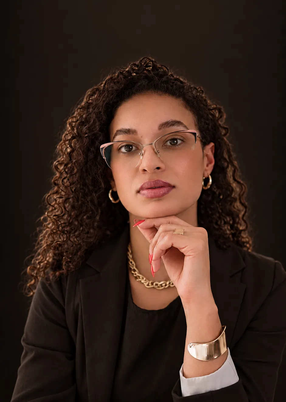 Sarajane Nunes, de óculos e blazer escuro, com a mão apoiada no queixo